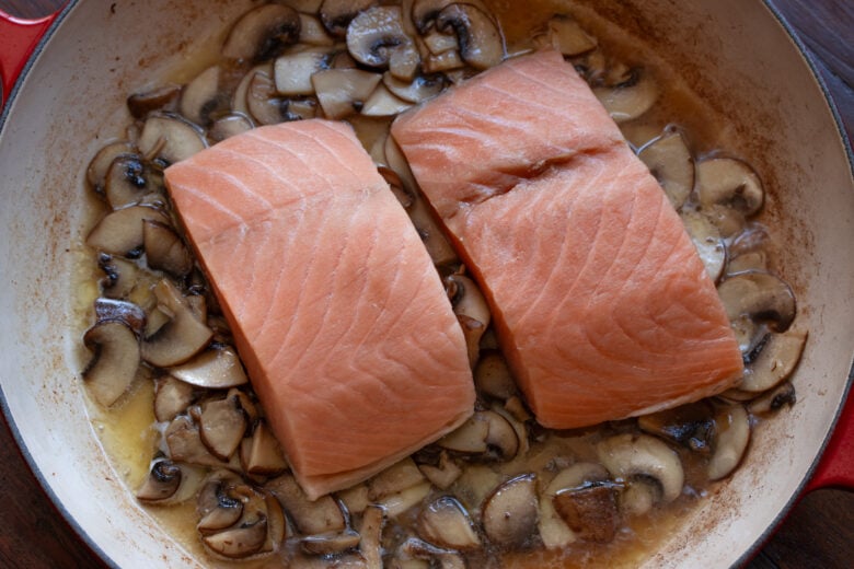 Salmon fillets placed over sautéed mushrooms.