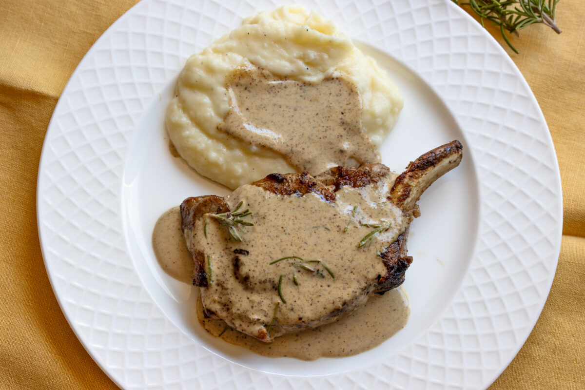 Mustard pork chops served in a plate with mashed potatoes and sauce all over them.