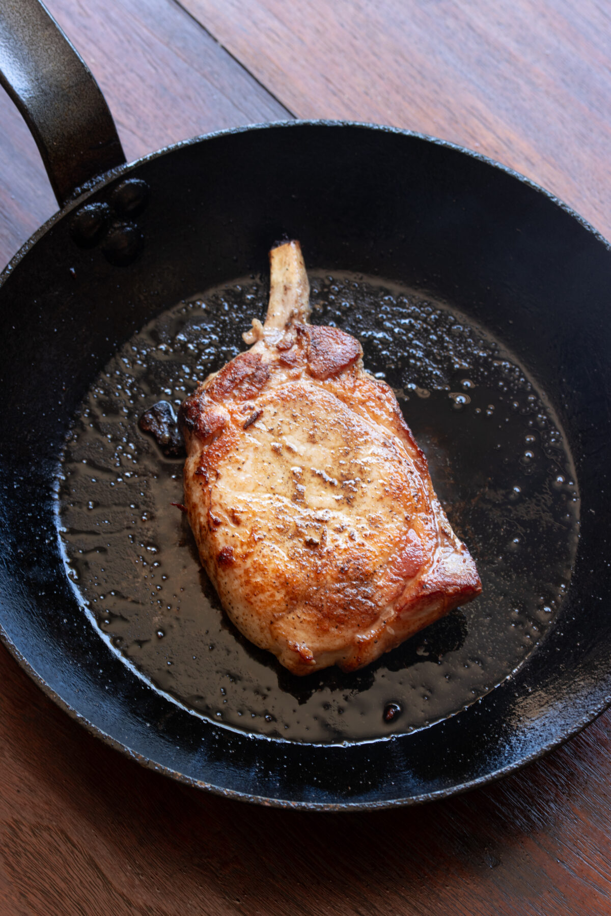 Pork chop seared in skillet with olive oil.