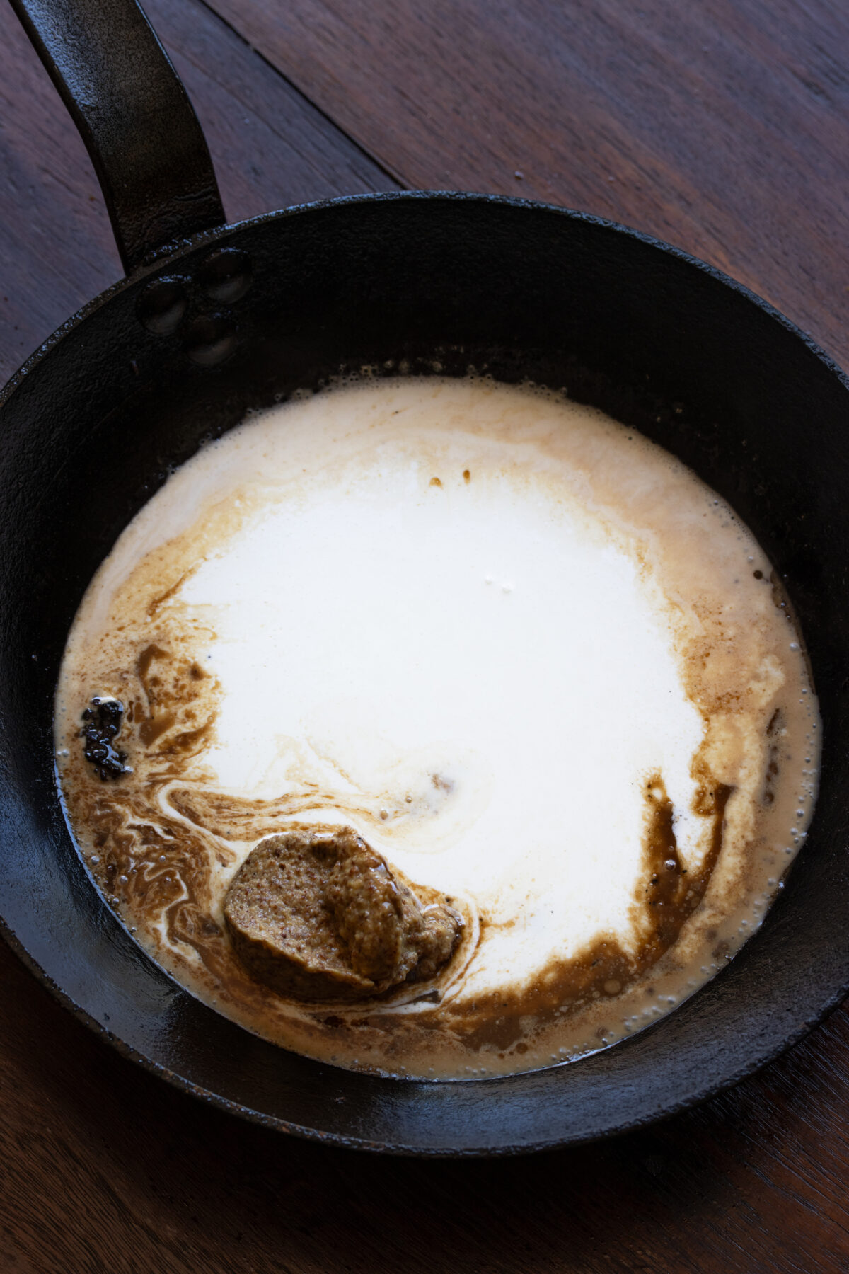 Adding dry white wine, heavy cream and whole grain mustard to the skillet.